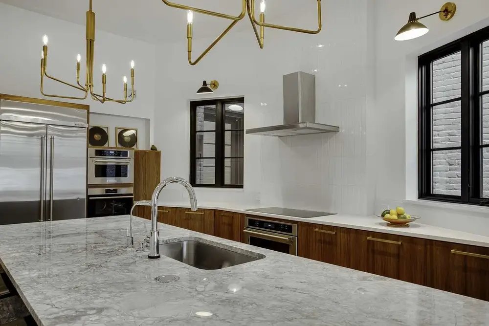 Modern kitchen with marble island, stainless steel appliances, wooden cabinets, and gold lighting – exploring if $10,000 is enough for a kitchen remodel.