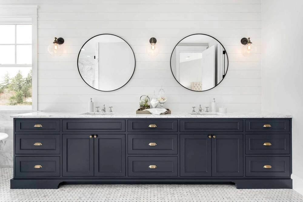 Modern double bathroom vanity with dark blue cabinets, white countertop, round mirrors, and wall sconces, representing a stylish bathroom setup related to “how much does it cost to install a bathroom vanity”.